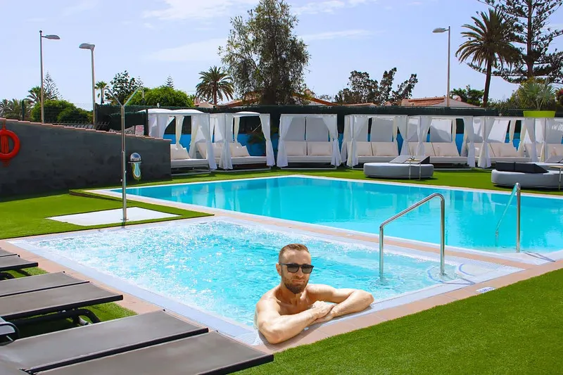Guest relaxing in the heated pool at Aqua Beach Bungalows, with daybeds and palm trees in the background.